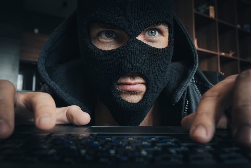 a man in a mask prints on the keyboard at a table in dark